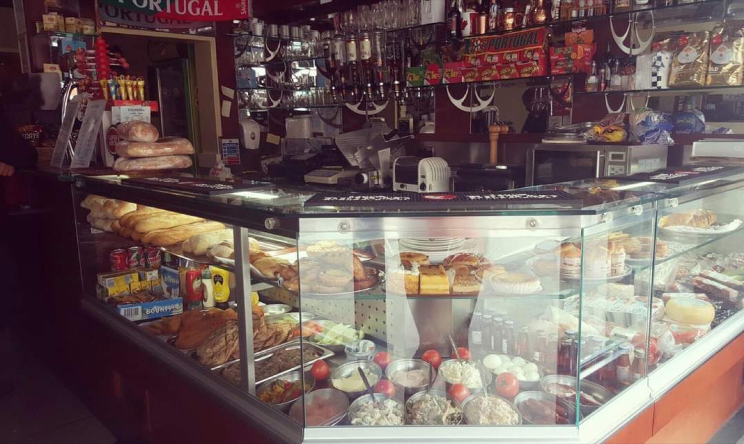 The deli counter at Palmeira, Leyton — fresh breads and pastries above trays of Portuguese salads, cured meats and groceries
