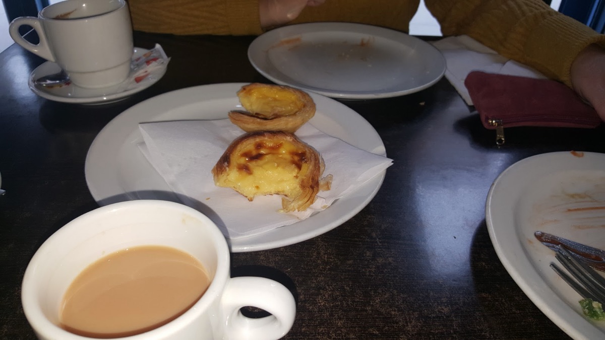 Two pastéis de nata custard tarts on a plate with Portuguese coffee